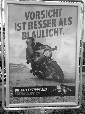 A person wearing protective gear is riding a motorcycle on a road with mountains in the background, accompanied by a German safety message about caution being better than blue lights and a website for safety tips.
Description generated by AI