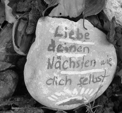 A stone with German text painted on it that reads "Liebe deinen Nächsten wie dich selbst" surrounded by leaves and natural debris.
Description generated by AI