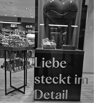 A store display features a large heart-shaped object and a sign with the German phrase Liebe steckt im Detail, surrounded by shelves of packaged goods.
Description generated by AI